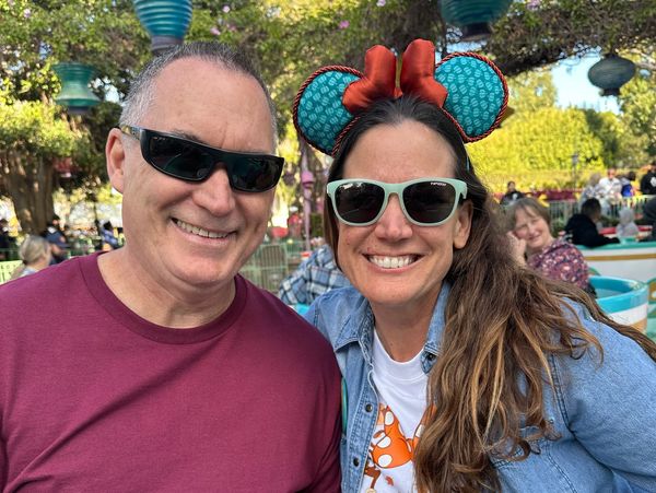 Smiling couple wearing sunglasses, enjoying a sunny day outdoors with festive decorations.