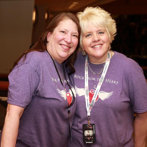 Two smiling women wearing matching purple 'Rock From The Heart' t-shirts.