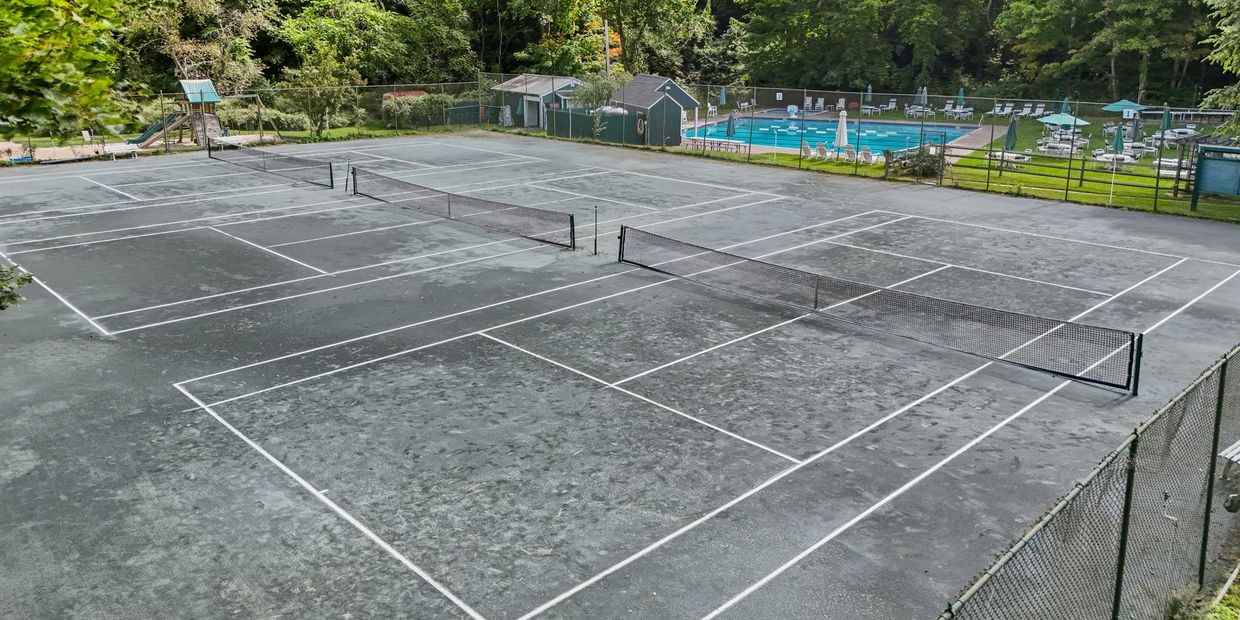Empty tennis courts with a swimming pool in the background.