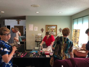 People browsing and selling jewelry at an indoor craft fair booth.