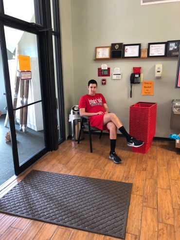 Young man in red outfit sitting on a chair inside a store near entrance.