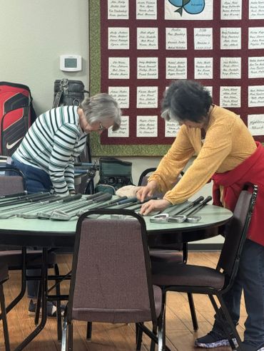 Two women examining metal rods on a round table indoors.