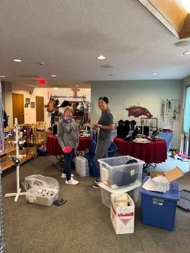 Two women organizing items in a room filled with tables and storage bins.