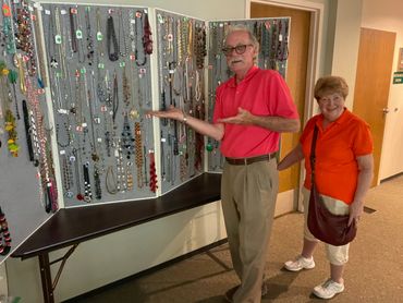 Two elderly people with a large display of jewelry on a folding board.