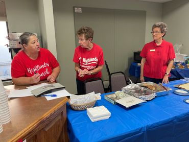 Three women in red shirts organizing food and money at a community event.
