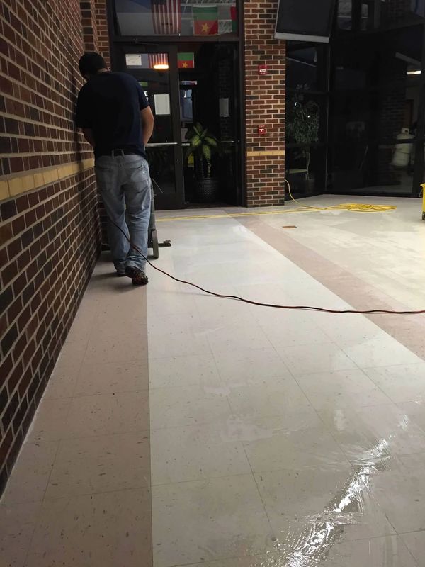 Man cleaning shiny tiled floor in hallway with brick walls.