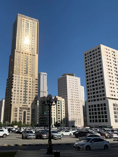 Tall buildings with a busy parking lot under clear blue sky.