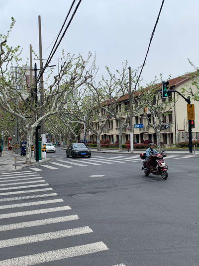 A quiet urban intersection with a pedestrian and vehicles under cloudy skies.