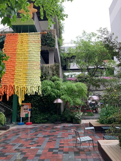 Colorful knitted decoration hanging in a lush urban courtyard with seating.