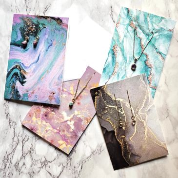 Necklaces displayed on colorful marbled cards on a marble surface.