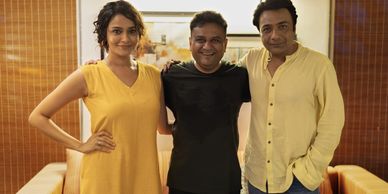 Three people posing happily indoors, two in yellow and one in black.