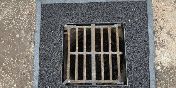 A metal grate over a drain on an asphalt surface.