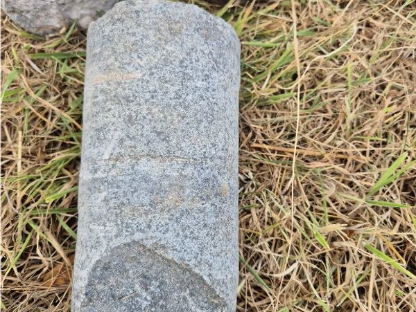 A weathered stone cylinder lying on dry grass.