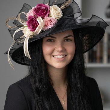 Smiling woman wearing a black hat adorned with pink and white roses.