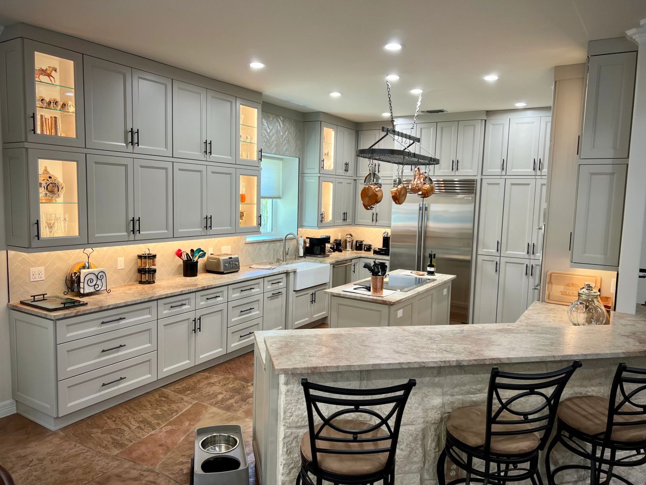Spacious modern kitchen with grey cabinets and copper pots.