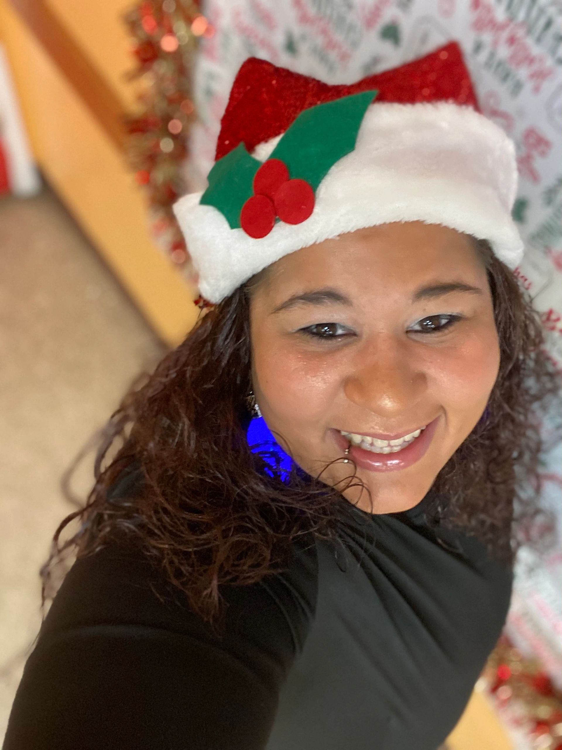 Smiling woman wearing a festive Christmas hat with holly decoration.