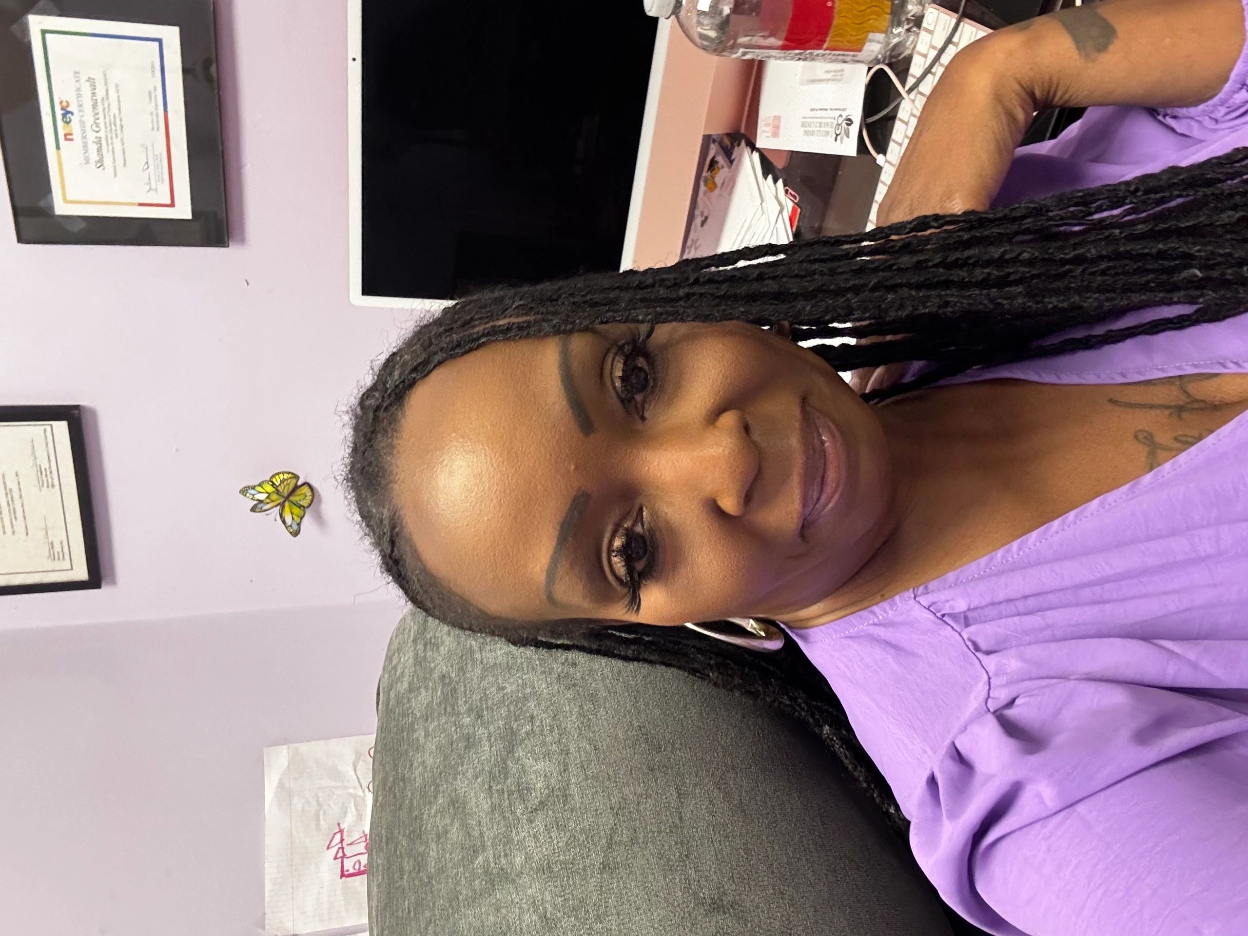 Woman with braided hair in purple blouse sitting in an office.