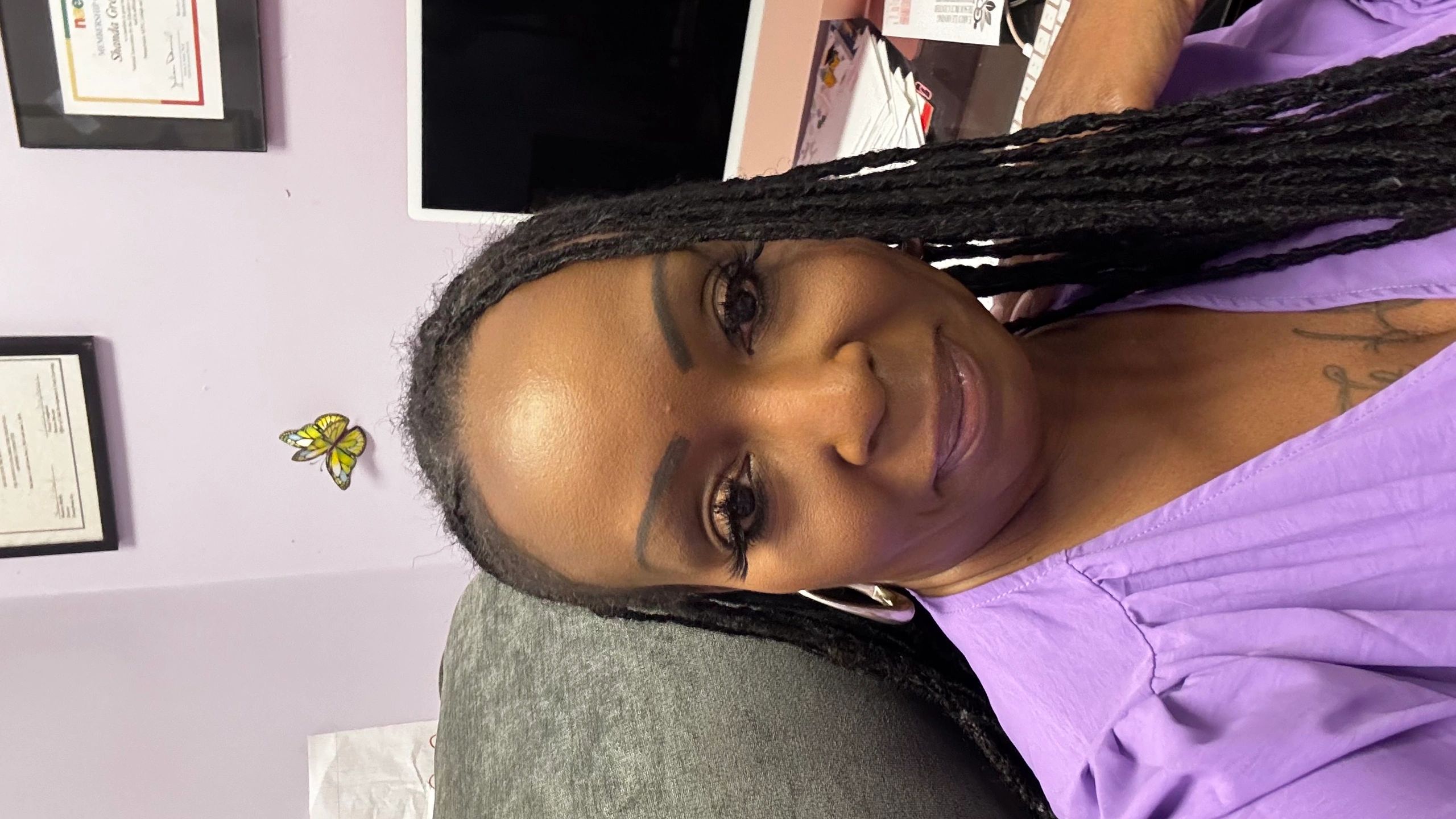 Woman with braided hair in purple blouse sitting in an office.