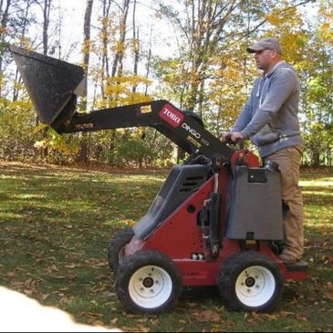 Man operating a compact Toro Dingo loader in a wooded area.
