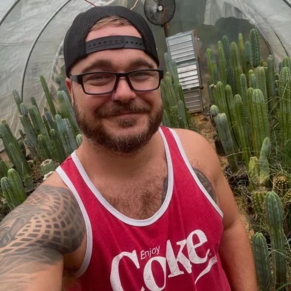Smiling man in a red Coke tank top in a cactus greenhouse.