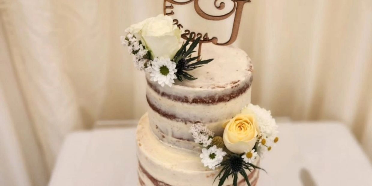 Two-tiered naked cake decorated with flowers and a wooden topper.