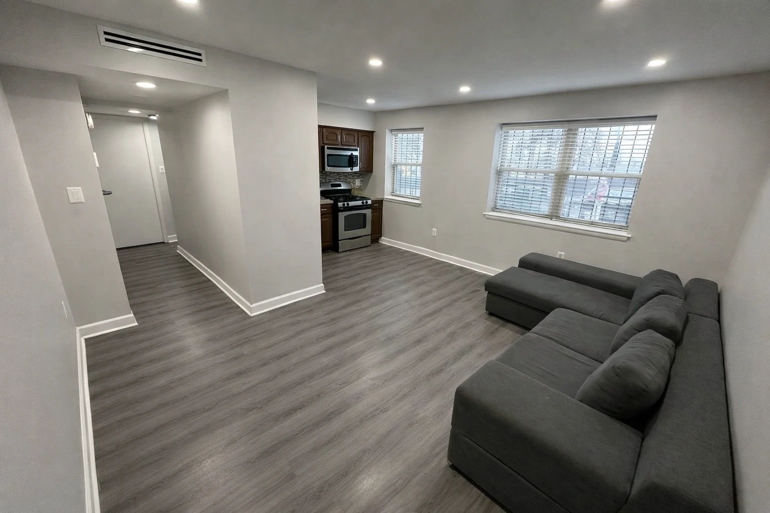Modern studio apartment with gray flooring and sectional sofa.