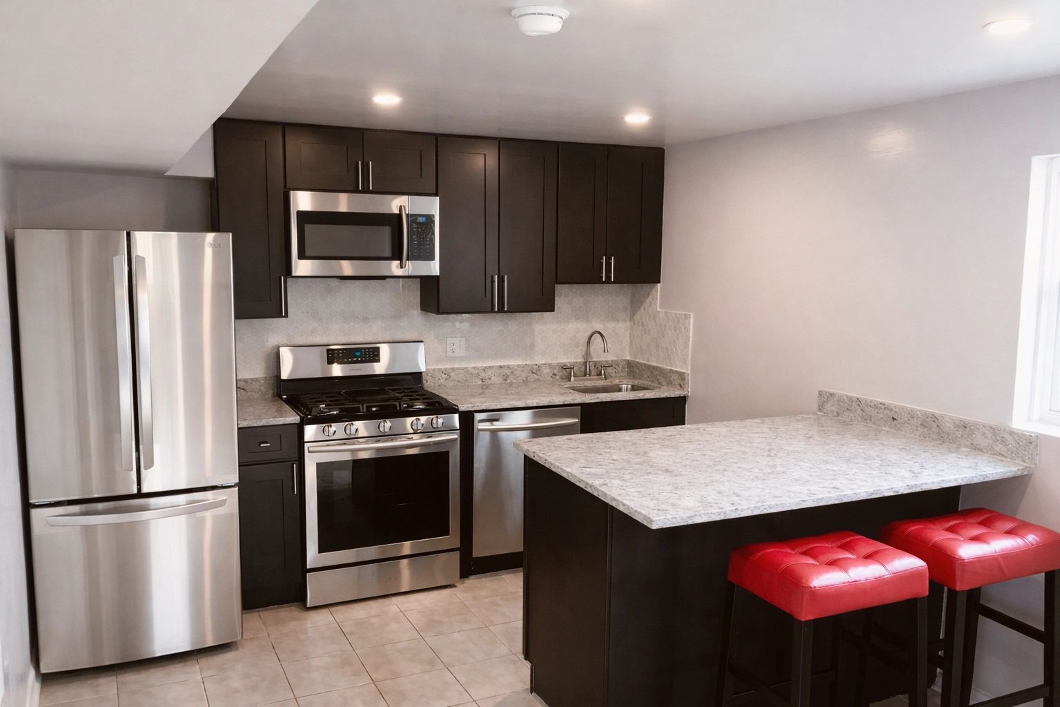Modern kitchen with stainless steel appliances and red cushioned stools.