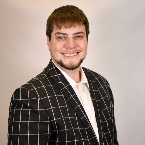 Smiling man in a black checkered blazer and white shirt.