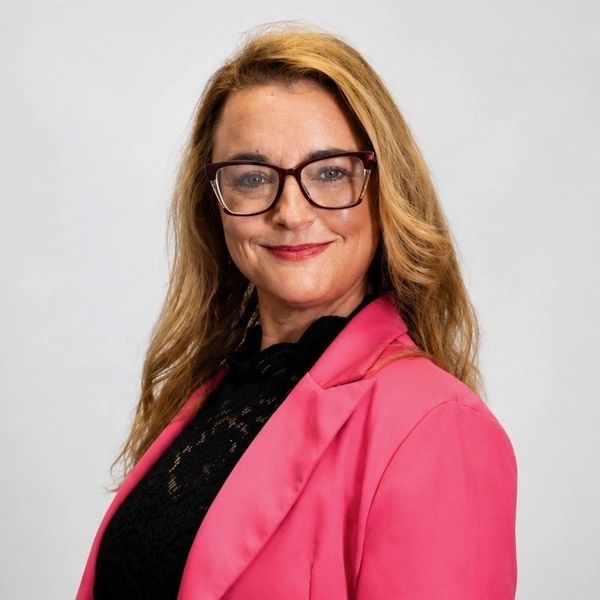 Confident woman in glasses wearing a pink blazer and black top.