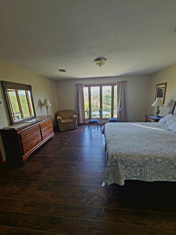 Spacious bedroom with wooden flooring, large bed, and seating area by glass doors.