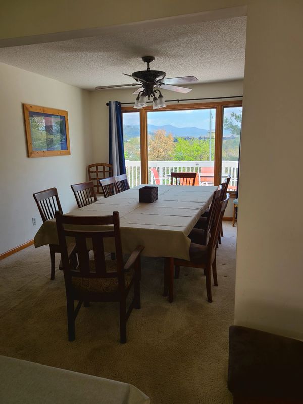 Dining room with a table, chairs, ceiling fan, and mountain view through glass doors.