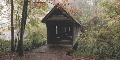 Covered bridge in misty autumn woods with fallen leaves and quiet forest path.