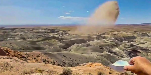 Person throwing sand into the air over a rocky desert.