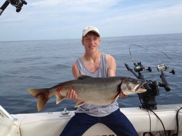 A young man holding a large fish on a boat in open water.