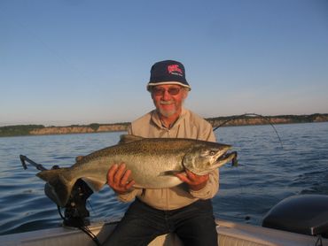 Man proudly holding a large fish on a boat in calm waters.