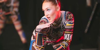 Performer in colorful patterned costume posing thoughtfully on stage.