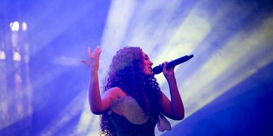 A female singer passionately performing on stage with colorful lights.