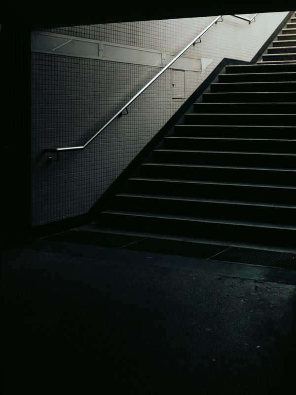 Dimly lit stairway with metal handrail and tiled wall.