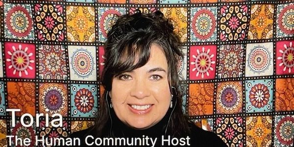 Portrait of Toria, the Human Community Host, smiling warmly against a colorful patterned backdrop.