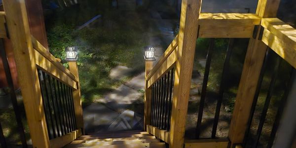 Well-lit wooden staircase leading to a backyard at night.