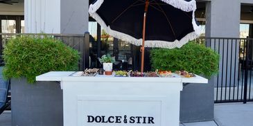 Outdoor Dolce & Stir cart with food and a fringed umbrella for corporate events, private event catering and wedding catering. 