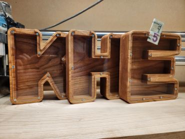 Wooden letters spelling 'KHE' on a table with a $5 bill on the letter E.