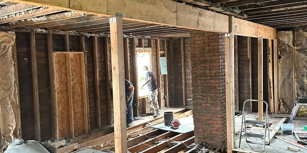 Construction workers renovating an exposed wooden framework inside a building.