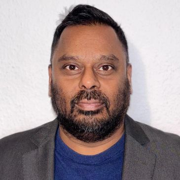 Portrait of a man with a beard wearing a blazer and blue shirt.