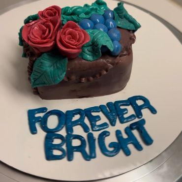 Small chocolate cake with red roses and blue grapes decoration.