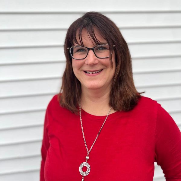 Smiling woman in red shirt with glasses and pendant necklace.