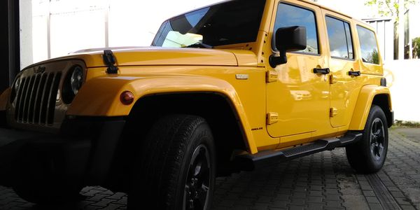 Yellow Jeep Wrangler parked on a paved surface.