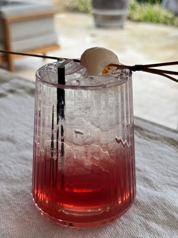 A refreshing red iced drink garnished with a lychee on a skewer.