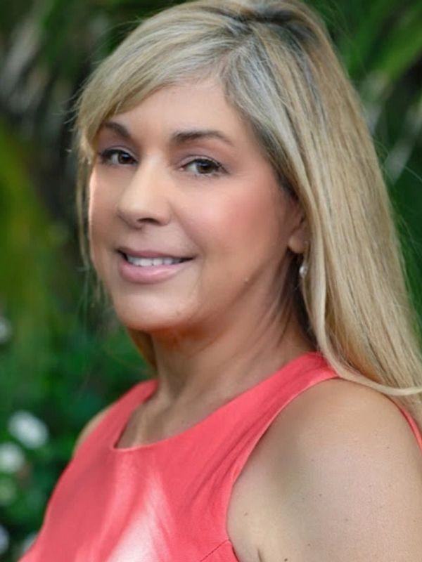 Smiling woman with blonde hair in coral dress outdoors.