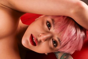 Close-up of a person with pink hair and red lipstick against a red background.